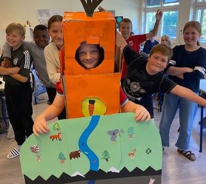 Bildet viser en gutt i et klasserom som er utkledd i et hjemmelaget gulrot-kostyme. Klassen til gutten står bak og smiler. Bildet er tatt i forbindelse med et prosjekt fra miljøagentene.