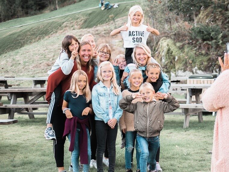 En gruppe barn smiler mot en fotograf. De står utendørs, og i bakgrunnen er det en ås. Noen av barna sitter på skuldrene til hverandre. De er medlem i Aktivitetsklubben.